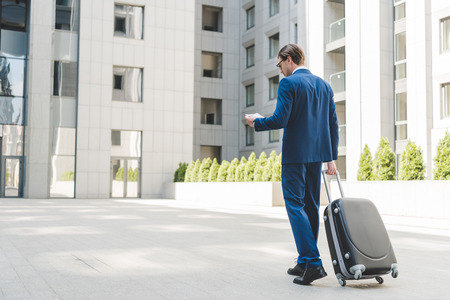 young businessman in stylish suit with luggage and flight tickets walking by business districtの写真素材