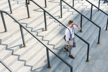 high angle view of stylish young man walking on stairs with laptop on city streetの写真素材