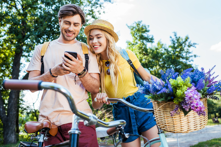 smiling couple using smartphone in park on summer dayの写真素材