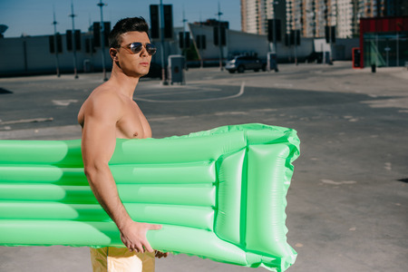 attractive young shirtless man with inflatable bed on parkingの写真素材