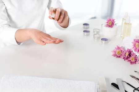 partial view of woman using aroma oil at table with towels, flowers, candles and instruments for manicure in beauty salonの写真素材
