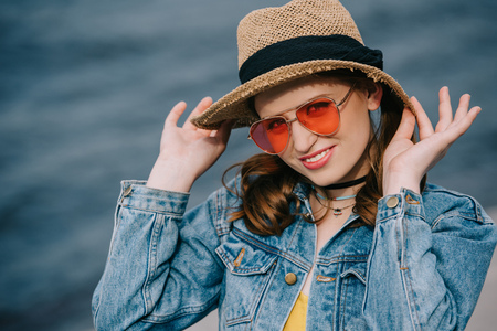 portrait of beautiful stylish young woman in hat and sunglasses smiling at camera outdoors