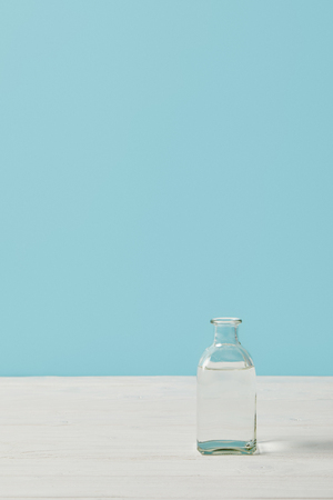 glass bottle of water on white tabletop isolated on blueの写真素材
