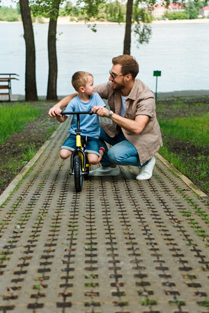 father and son with small bike looking at each other at parkの写真素材