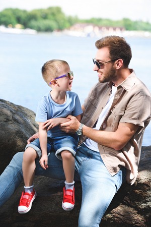 happy father and son looking at each other on stones near riverの写真素材