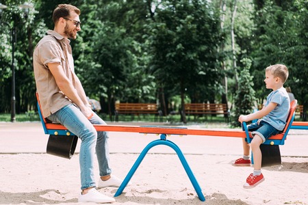 side view of father and son having fun on swing at playground in parkの写真素材
