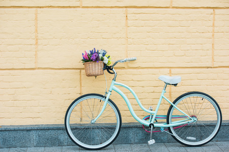white bicycle with beautiful colorful flowers in basket near wall