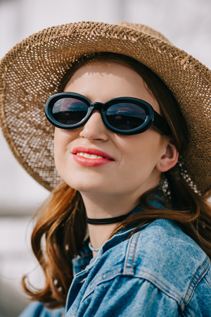 portrait of happy young woman in sunglasses, hat and denim jacket smiling outdoorsの写真素材