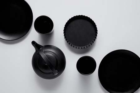 top view of black teapot, plates, baking dish and cups on white tableの写真素材