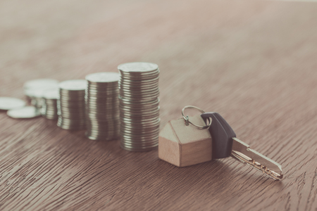 key with trinket near stacks of coins on wooden table, saving conceptの写真素材