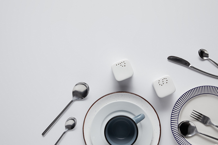 top view of saltcellar, pepper caster, spoons, knife, fork, cup and plates on white tableの写真素材