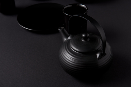 selective focus of black teapot, cups and plate on black tableの写真素材