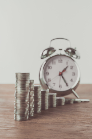 stacks of coins and alarm clock on wooden table, saving conceptの写真素材