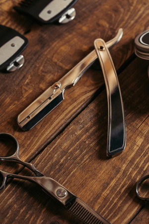 close-up view of straight razor and scissors on wooden surface in barbershopの写真素材