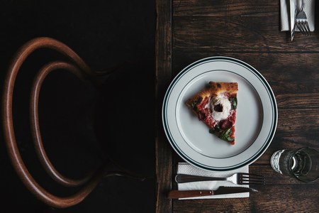 top view of delicious pizza slice on plate with setting and on rustic wooden tableの写真素材