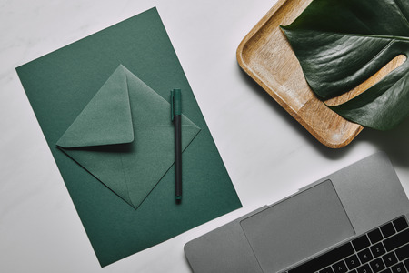 Green paper for letter template by laptop on white marble background