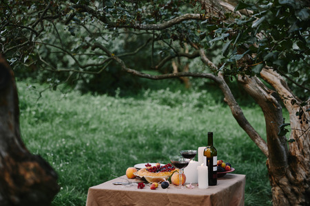 candles, glasses with wine and pie on table in gardenの写真素材