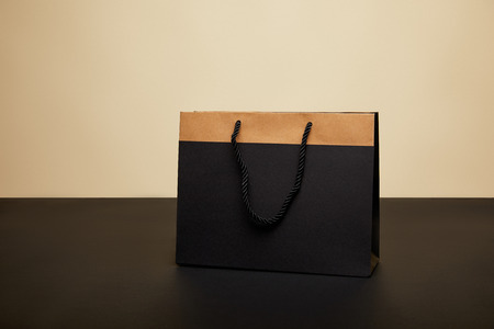 one black shopping bag on black table isolated on beigeの写真素材