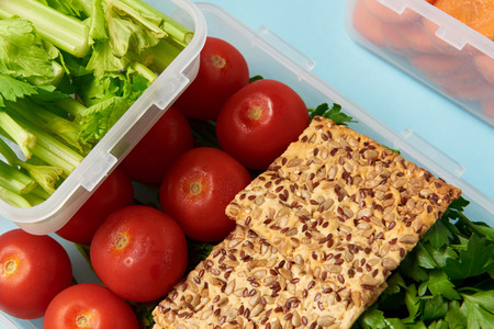 close up view of arrangement of food containers with fresh vegetables and cookies isolated on blue