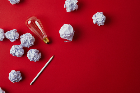 top view of crumpled papers with light bulb and pencil on red surfaceの写真素材