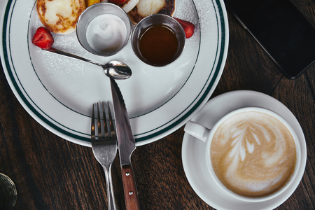 top view of delicious curd pancakes on plate with cup of coffee and smartphone on rustic wooden...