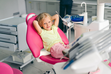 smiling kid looking at camera awhile sitting in chair at dentist officeの写真素材