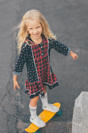 excited little kid looking at camera and riding on skateboard at streetの写真素材