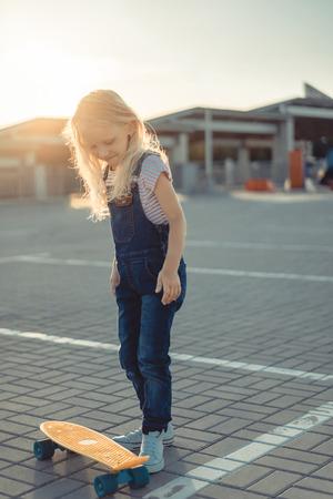 smiling adorable child standing with penny board at parking lotの写真素材