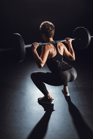 rear view of sportswoman exercising with barbell, black backgroundの写真素材