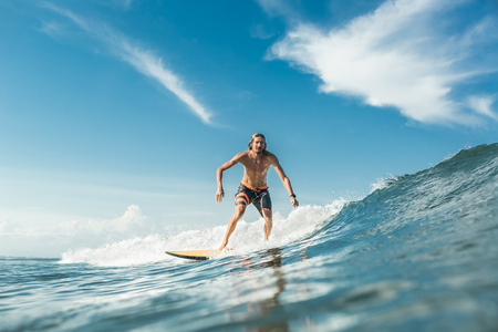 shirtless male surfer riding waves in ocean at Nusa Dua Beach, Bali, Indonesiaの写真素材