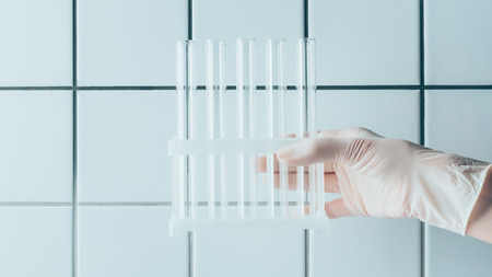 cropped shot of doctor holding test tubes in stand in front of tiled white wall