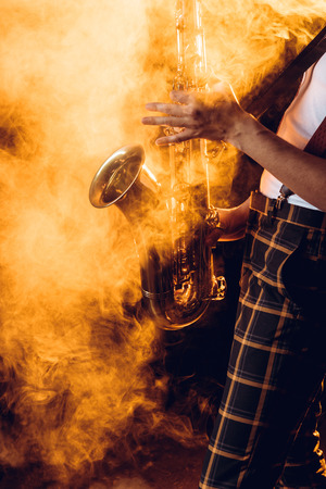 cropped shot of expressive young musician playing saxophone in smokeの写真素材