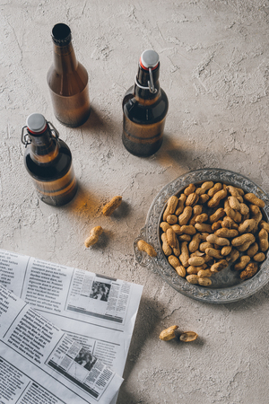 top view of peanuts, newspapers and bottles of beer arranged on concrete tabletopの写真素材