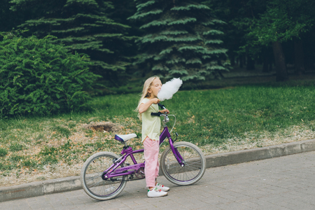side view of adorable kid with bicycle eating cotton candy in parkの写真素材