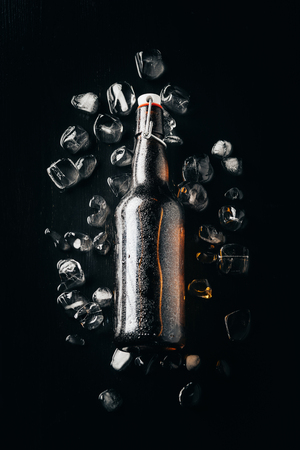 flat lay with glass bottle of beer on ice cubes arranged on dark tabletopの写真素材