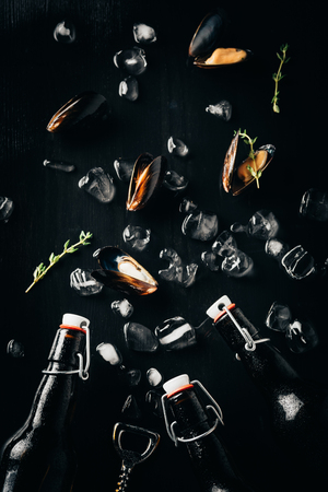 flat lay with bottle opener, bottles of beer, mussels and ice cubes arranged on dark tabletopの写真素材