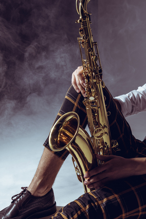 cropped shot of stylish musician holding saxophone in smoke on greyの写真素材