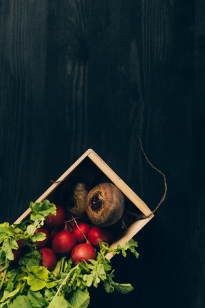 top view of radishes and beetroots in wooden box on grey dark tableの写真素材
