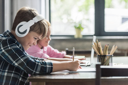 side view of smiling little schoolboy drawing with color pencils while his sister using laptopの写真素材