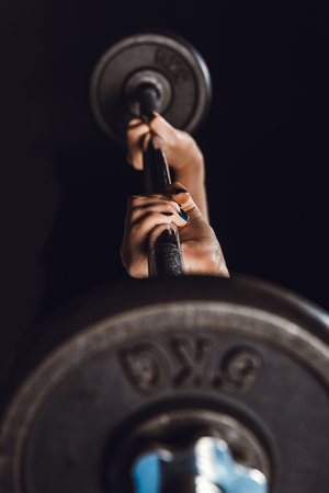 partial view of female athlete doing exercise with barbell at gym, black backgroundの写真素材
