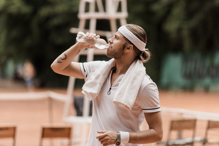 side view of handsome retro styled tennis player drinking water at tennis courtの写真素材