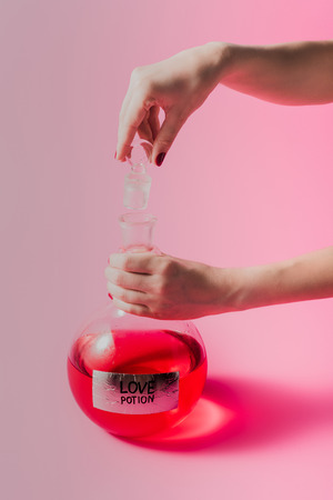 cropped shot of woman opening flask with red colored love potion on pink surface
