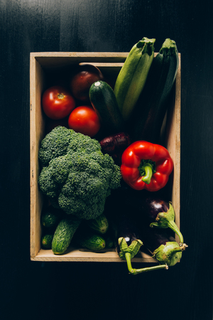 top view of zucchini, broccoli and eggplants in wooden box on dark tableの写真素材