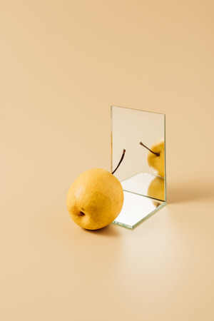 delicious yellow pear reflecting in two mirrors on beige tableの写真素材