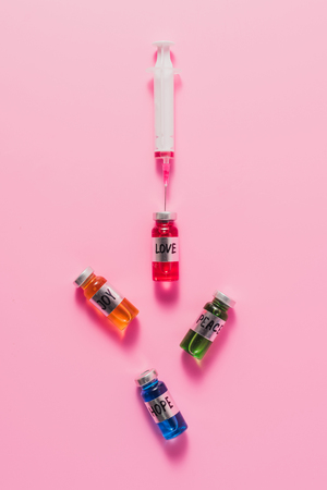 top view of syringe and bottles with love, hope, joy and peace vaccine signs on pink tabletopの写真素材