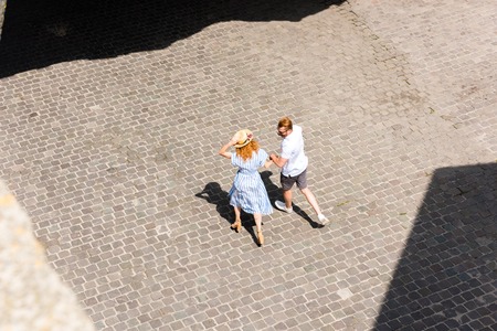 high angle view of redhead woman in straw hat walking and holding hand of boyfriend at city streetの写真素材