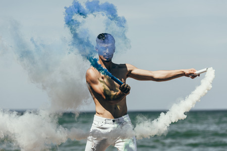attractive man holding blue and white smoke sticks in front of seaの写真素材