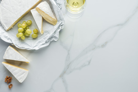 flat lay with glass of wine, camembert cheese and grape on white marble surfaceの写真素材