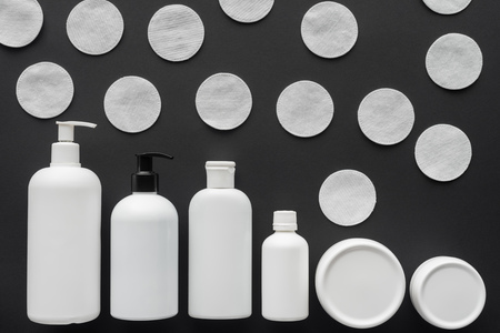 top view of bottles of cream and cosmetic cotton pads isolated on black, beauty conceptの写真素材