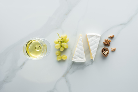 flat lay with glass of wine, camembert cheese and hazelnuts on white marble surfaceの写真素材
